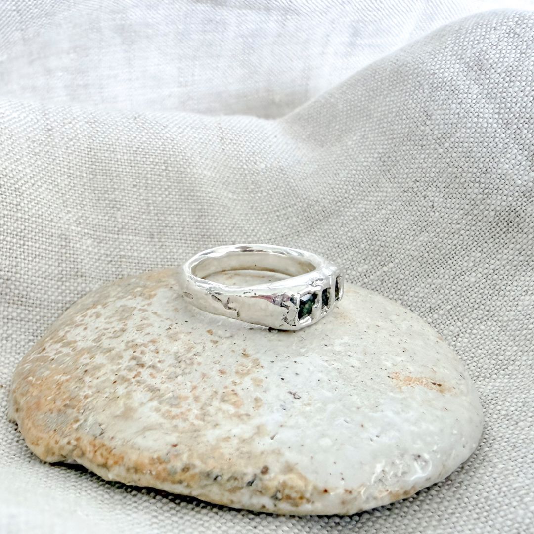 Side view of the Kākāriki sterling silver signet ring resting on a pale ceramic dish, showing the tapering band and organic textured finish.