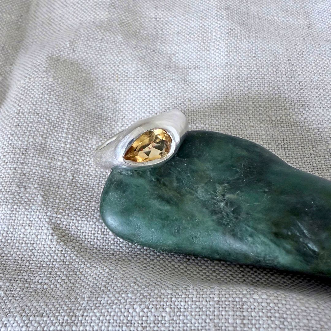 Sterling silver Kōwhai Signet Ring with natural citrine resting on pounamu