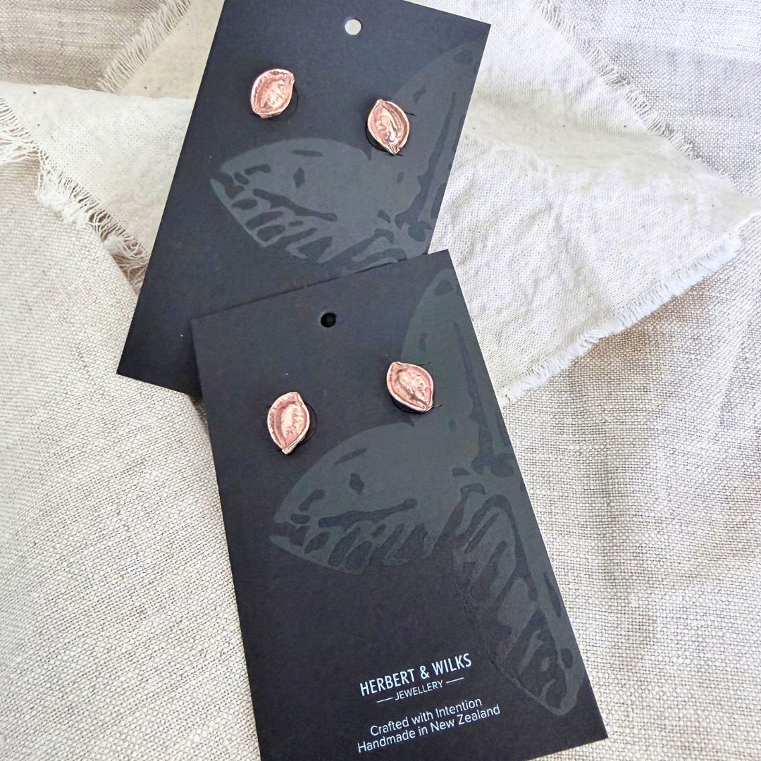 Two pairs of bronze Kōwhai Pod stud earrings displayed on black Herbert & Wilks jewellery cards.