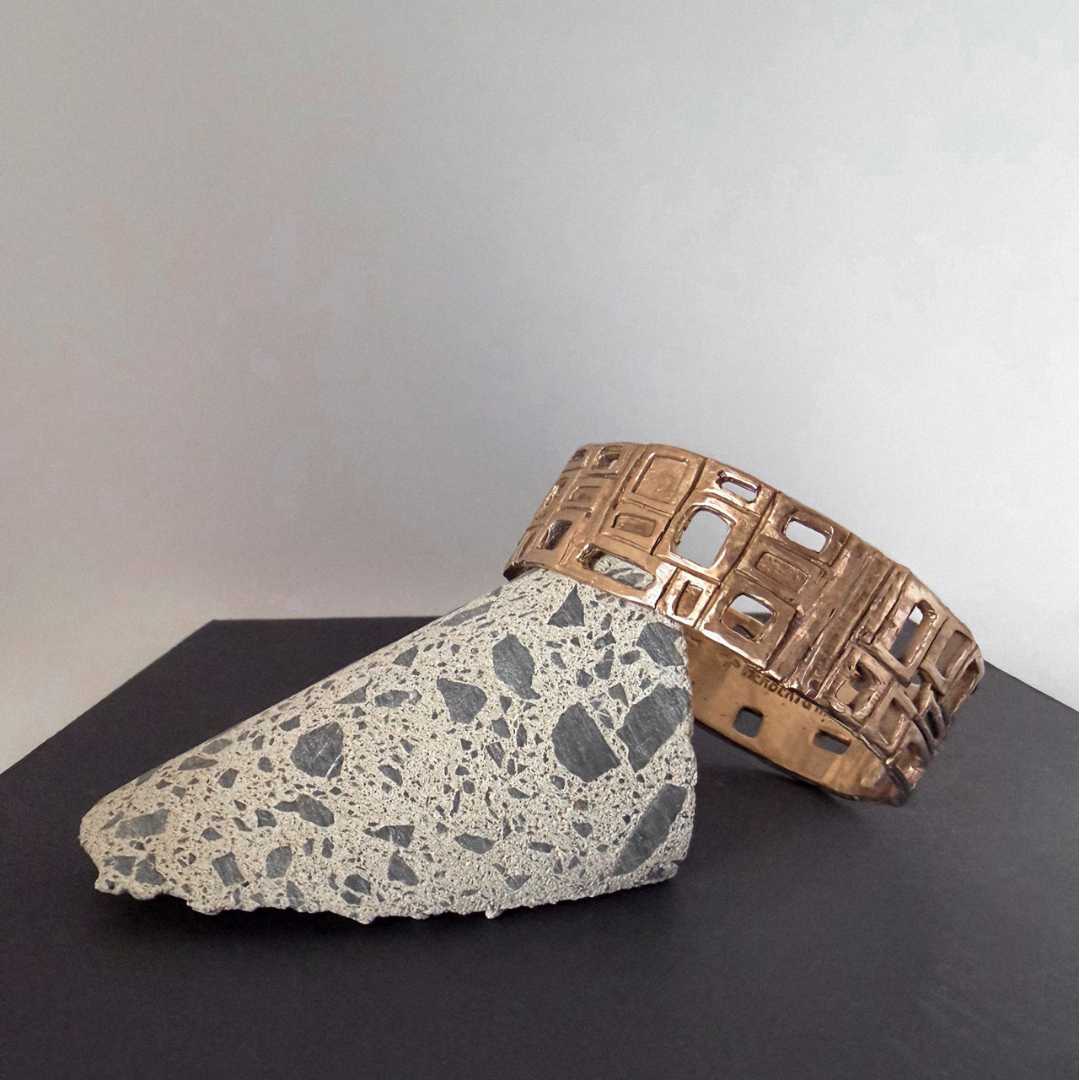 Modernist Bangle by HerbertandWilks in warm, caramel-toned solid bronze, resting against a textured concrete wedge.
