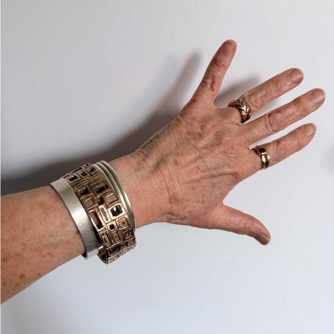 Modernist Bangle by HerbertandWilks in warm, caramel-toned solid bronze, styled in a mixed metal stack with silver cuffs and chains