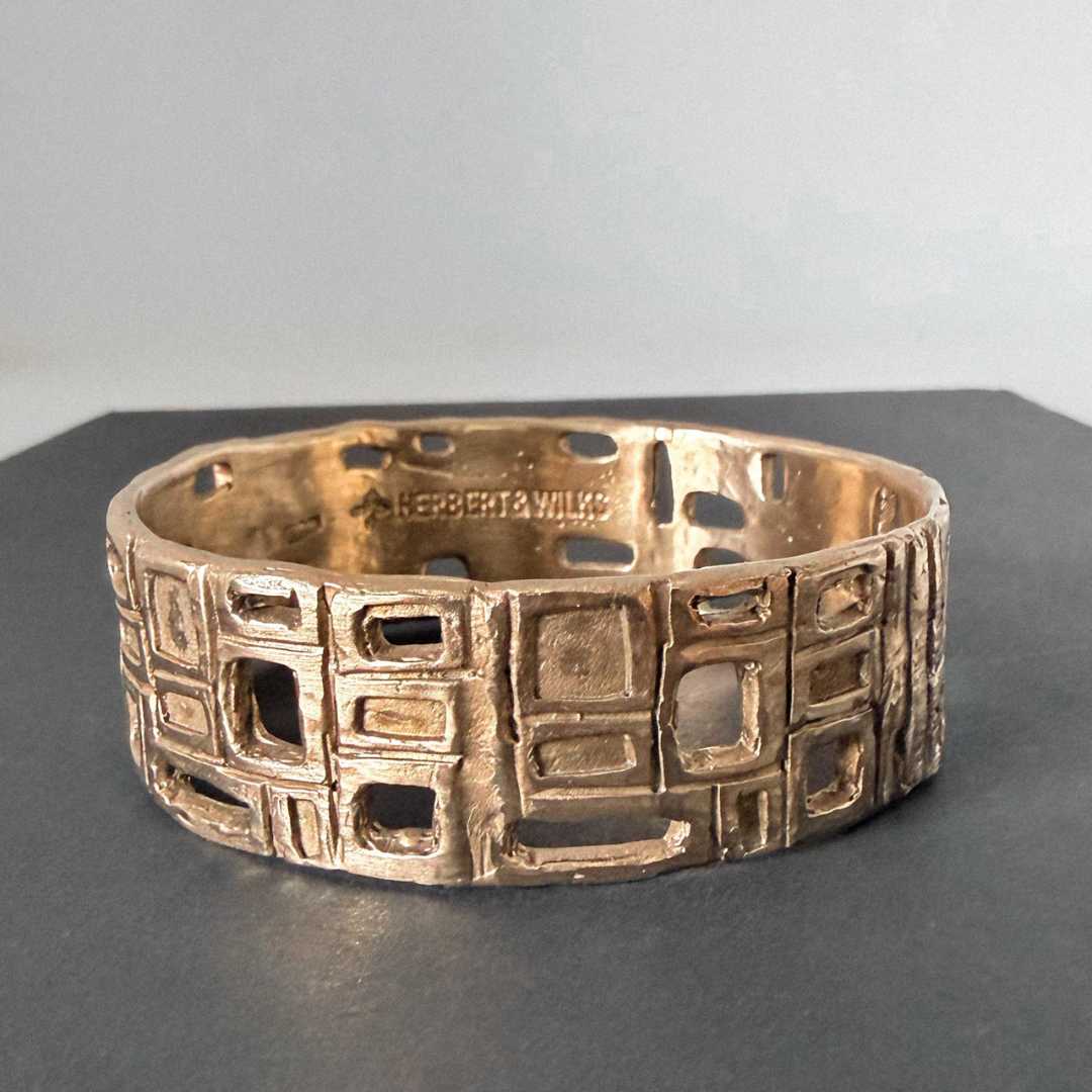 HerbertandWilks Modernist Bangle in warm, caramel-toned bronze, lying flat to showcase its sculptural texture and geometric design on a black surface