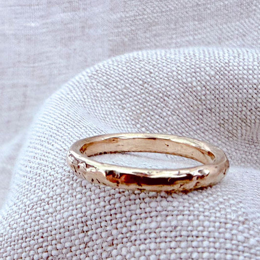 Handmade 9ct yellow gold Molten Ring with an irregular, organically textured surface and polished finish, resting on natural linen.