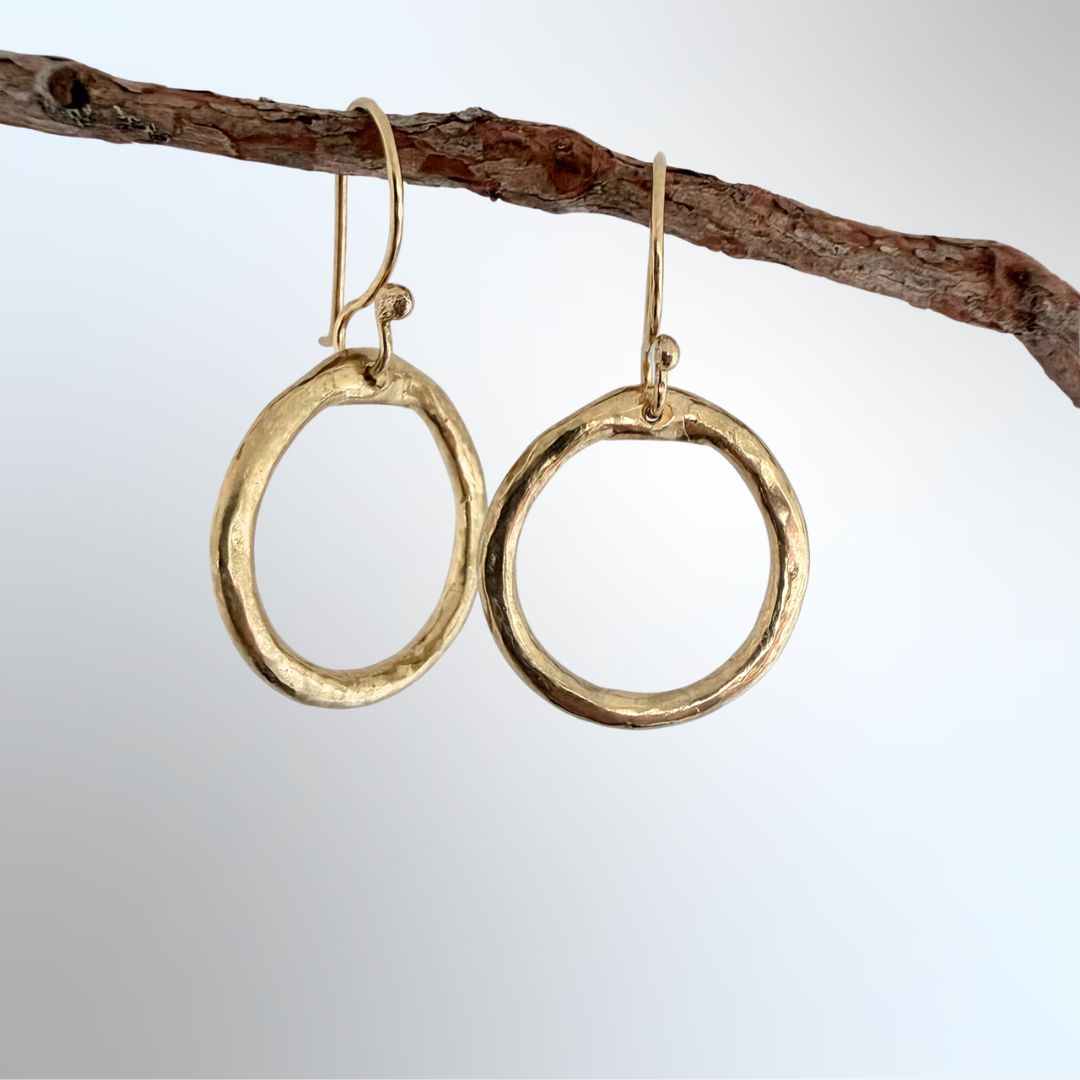 Organic Circle Hoop Earrings in 18ct gold plate hanging from a branch, one hoop at a slight angle, light grey-blue background — HerbertandWilks