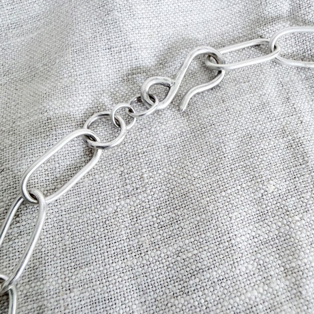 Close-up of handmade sterling silver hook clasp and oval links on the HerbertandWilks Oval Link Chain, photographed on textured natural linen.