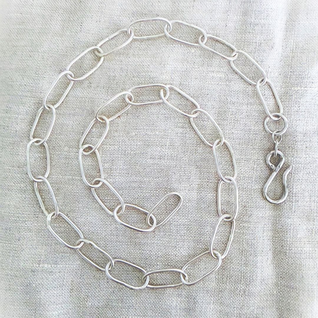 Sterling silver Oval Link Chain arranged in a spiral on linen, showing individually handmade oval links and a sculptural silver hook clasp.