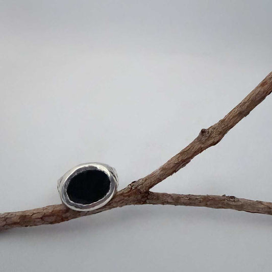 Oval Bloodstone Signet Ring in sterling silver propped against a branch, face-on, against a light blue-grey background — HerbertandWilks Jeweller
