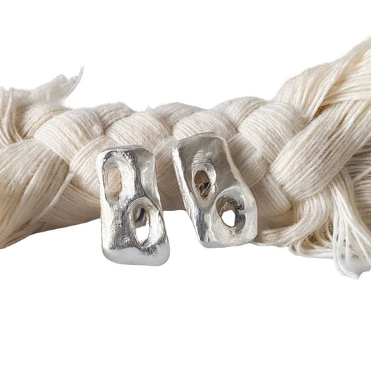 Sterling silver Perfora Rectangle Stud Earrings resting on a braided rope against a white background, showing sculptural pierced detail.