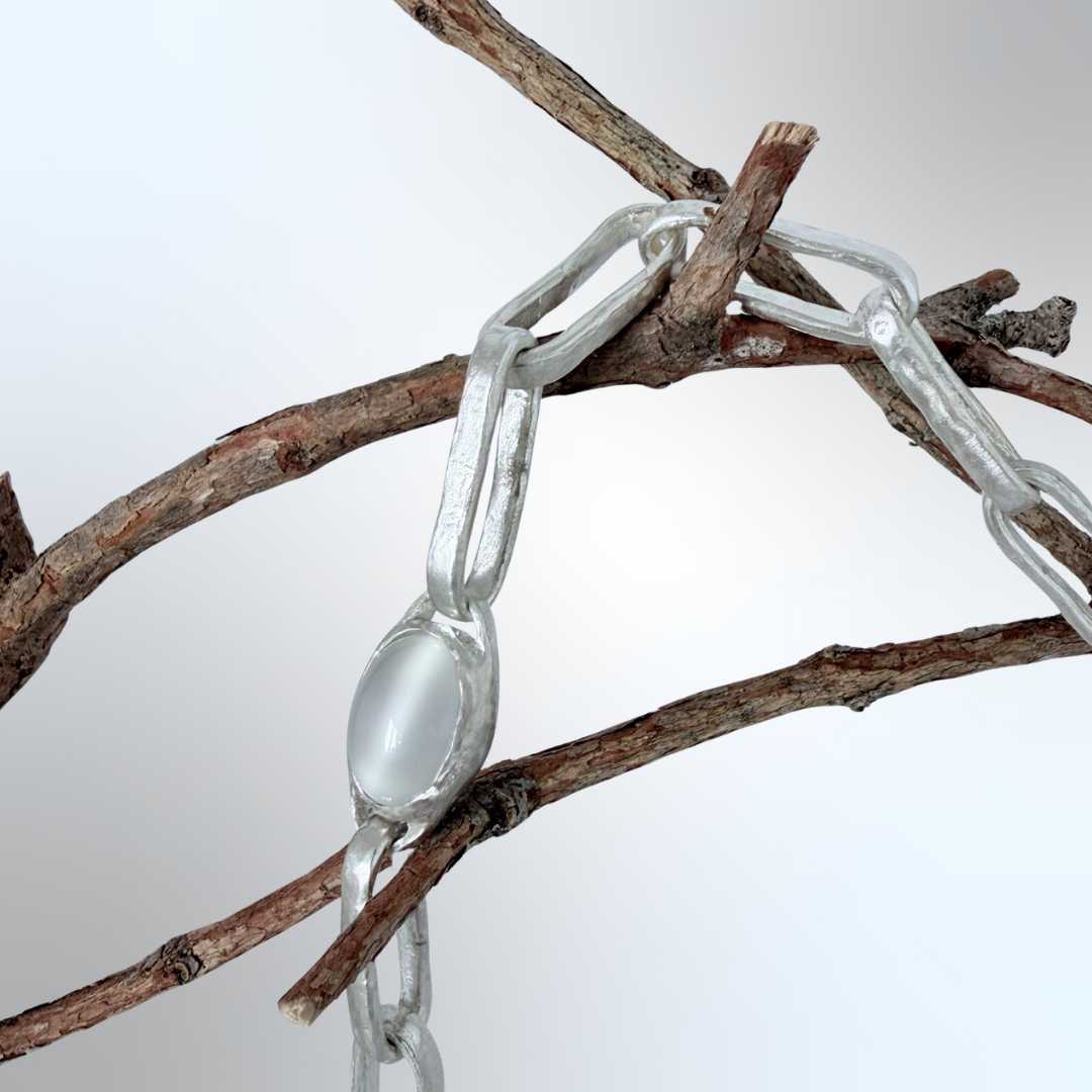Close-up of hand-fabricated open-back moonstone bezel and oversized obround sterling silver links draped over branches — handmade in Mt Eden, Auckland