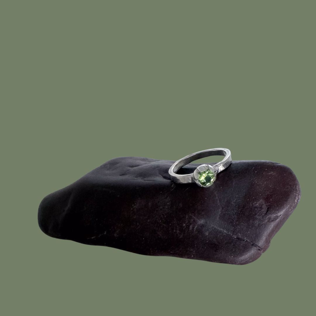 Peridot Bloom Stacking Ring in sterling silver, displayed on a dark polished stone against a solid olive green background.