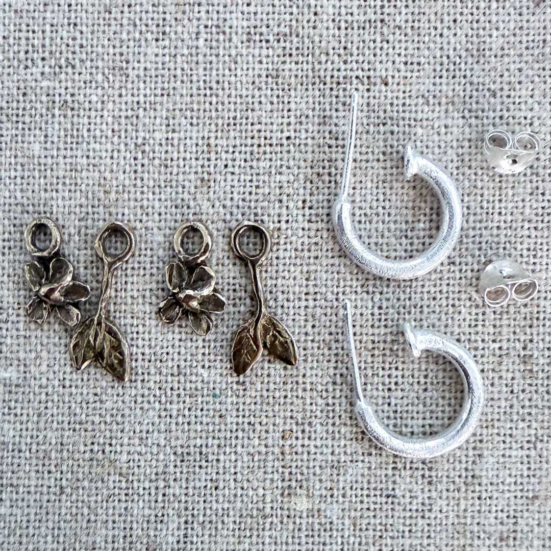 Handcrafted mixed metal Plum Blossom & Leaf earring full set bundle by HerbertandWilks Jewellery. Includes two bronze flower charms, two bronze leaf charms, and textured sterling silver hoops, displayed on a textured beige linen background. Local Auckland jewellery.