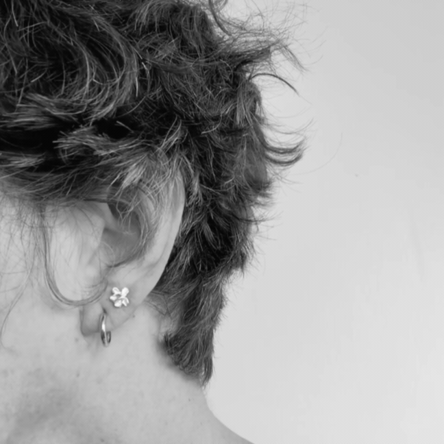 Sterling silver plum blossom stud earring worn in a second piercing above a pair of textured gold hoop earrings.