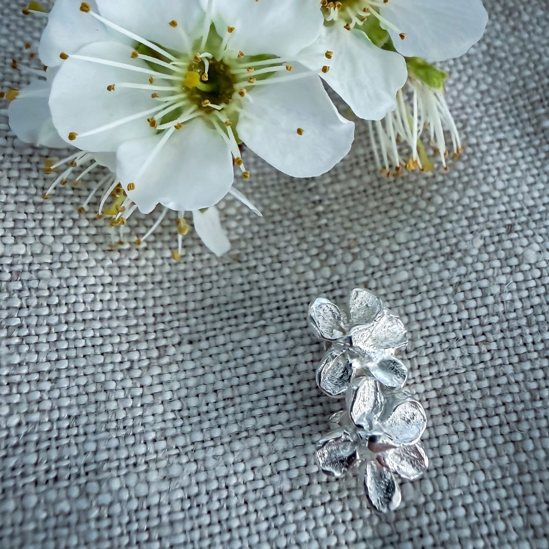 Sterling silver plum blossom stud earrings arranged beneath fresh white plum blossoms on textured natural linen.