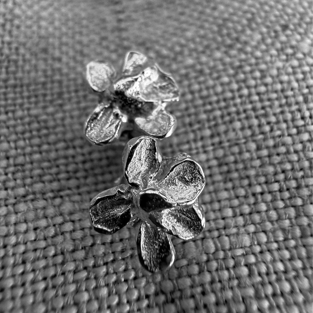 Close-up of two textured sterling silver plum blossom stud earrings showing their irregular sculptural petals.