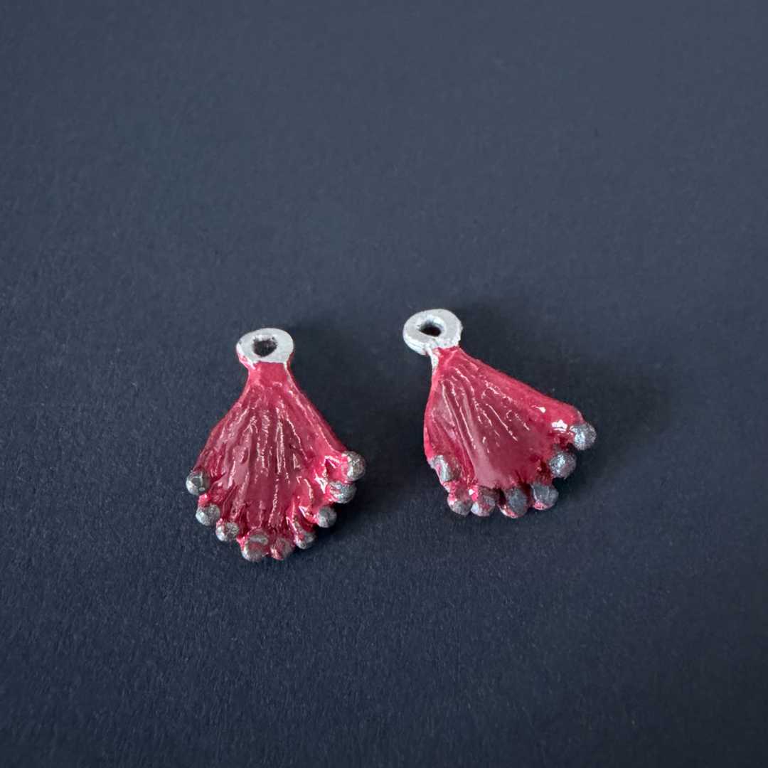 Pair of hand-carved sterling silver Pohutukawa flower charms featuring red enamel petals and oxidised stamen tips. Shown without sleepers on a black background.