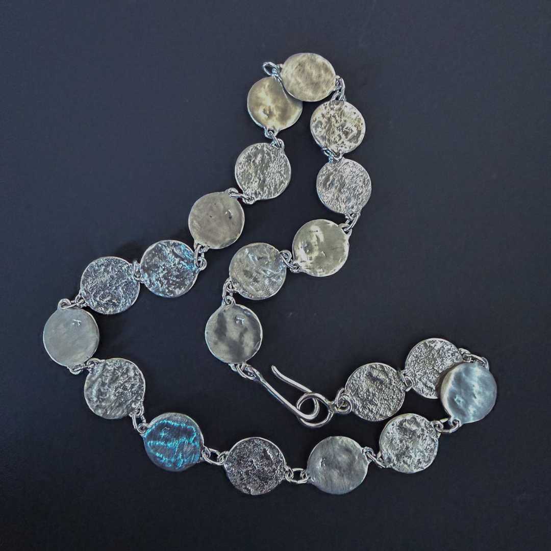 Detailed view of the solid sterling silver findings, clasp, and textured elements of the Sequin Disc Necklace against a dark background