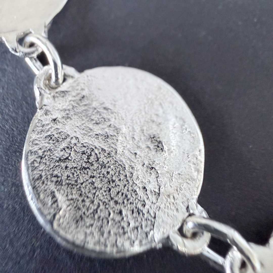 rtistic macro shot of a sterling silver disc and chain links from the Sequin Disc Necklace against a dark background, highlighting the organic hand-finished texture with a soft, shallow focus.