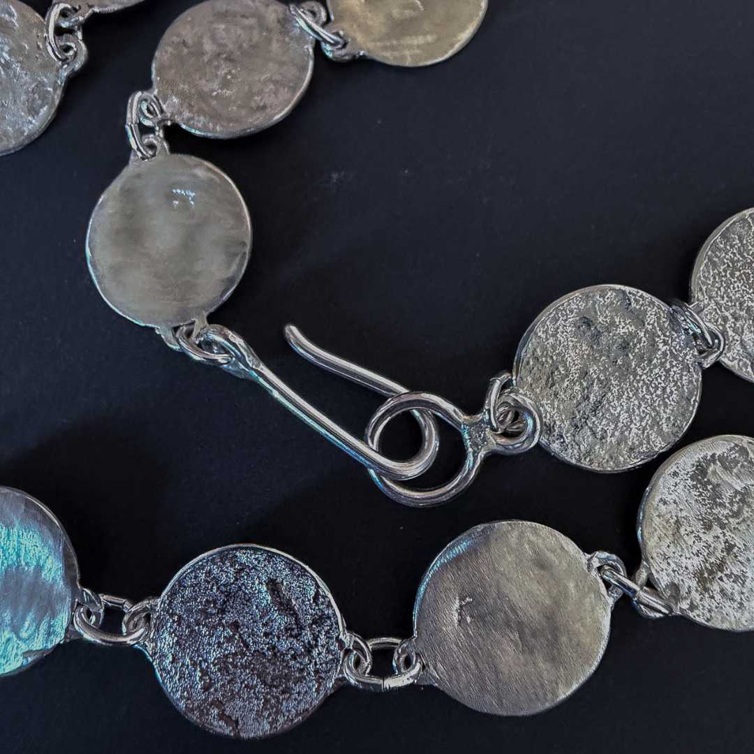 Close-up detail of the sterling silver Sequin Disc Necklace on a dark background, highlighting the intricate hand-reticulated and polished textures of the individual silver discs.
