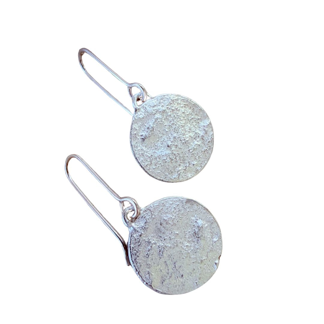 A pair of Sequin Swing Earrings which have a signature textured sterling silver disc with fishhook wires, displayed against a solid white background.