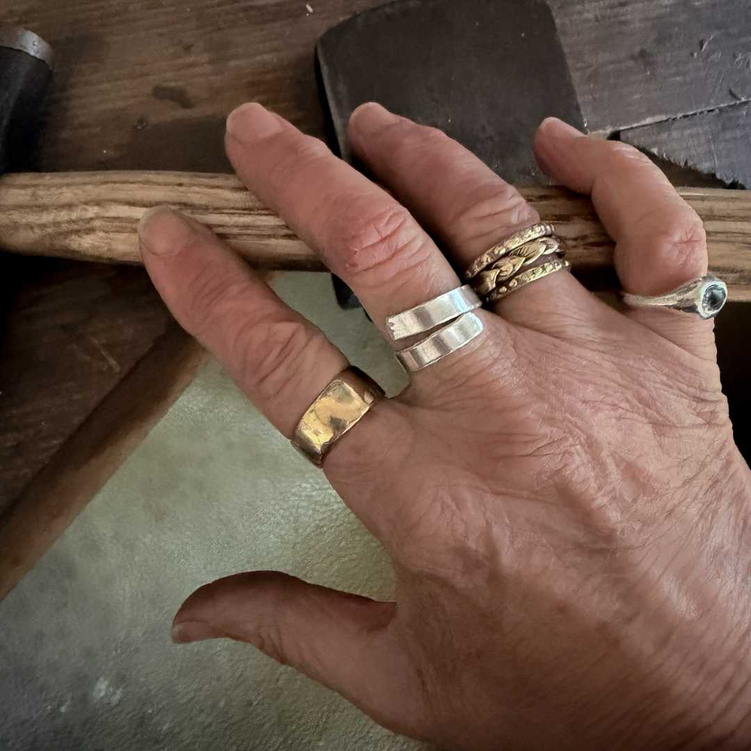 A makers hand wearing multiple rings including the solid sterling silver open ring on a wooden surface