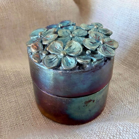 Small cylindrical bronze Hydrangea Box with heat-patinated finish and hand-carved hydrangea flowers covering the lid.
