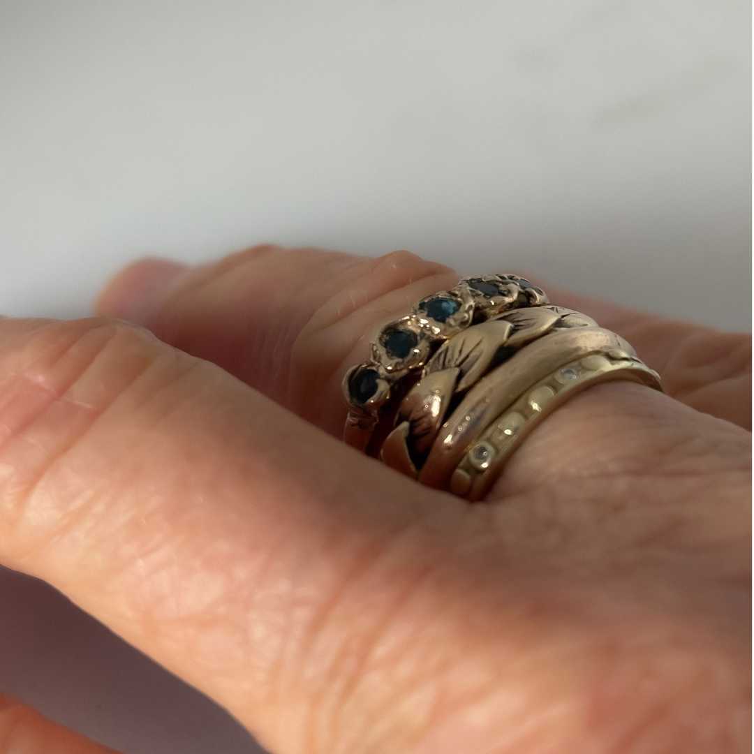 Stack of handmade textured gold rings showing sandcast grain, carved leaves, fluid forms and sapphire-set surface detail