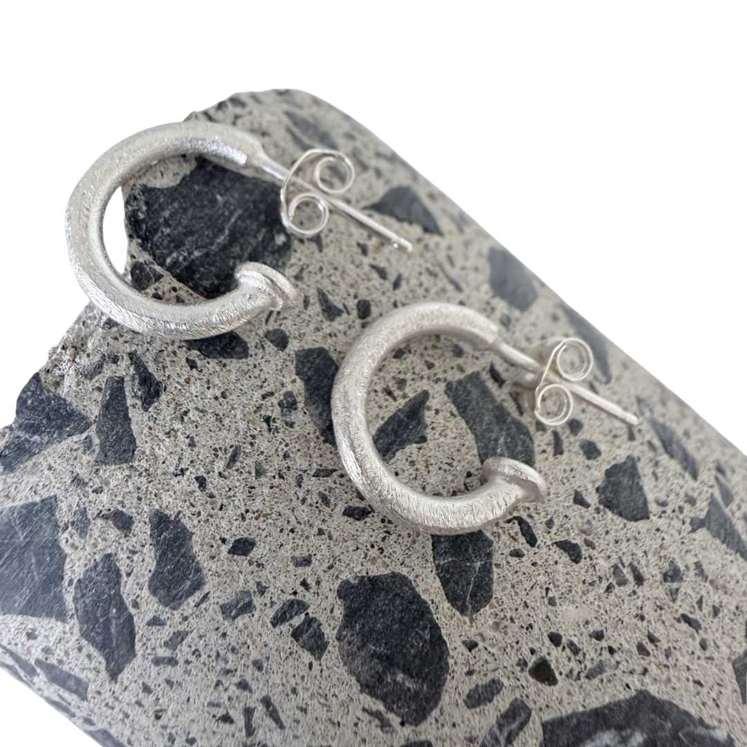 13mm textured sterling silver hoop earrings lying on cut concrete surface showing stone chip detail viewed from above