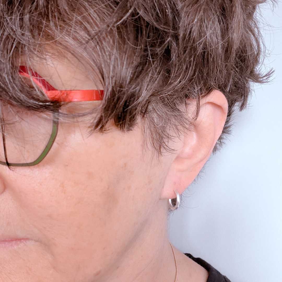 Woman with short hair wearing 13mm textured sterling silver hoop earrings against a light blue background