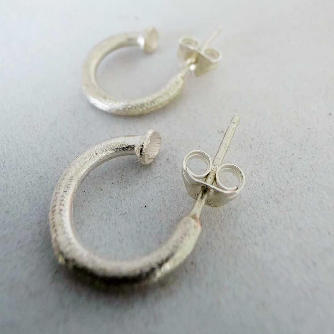 Close-up of 13mm textured sterling silver hoop earrings lying on grey surface showing detailed hand-finished texture