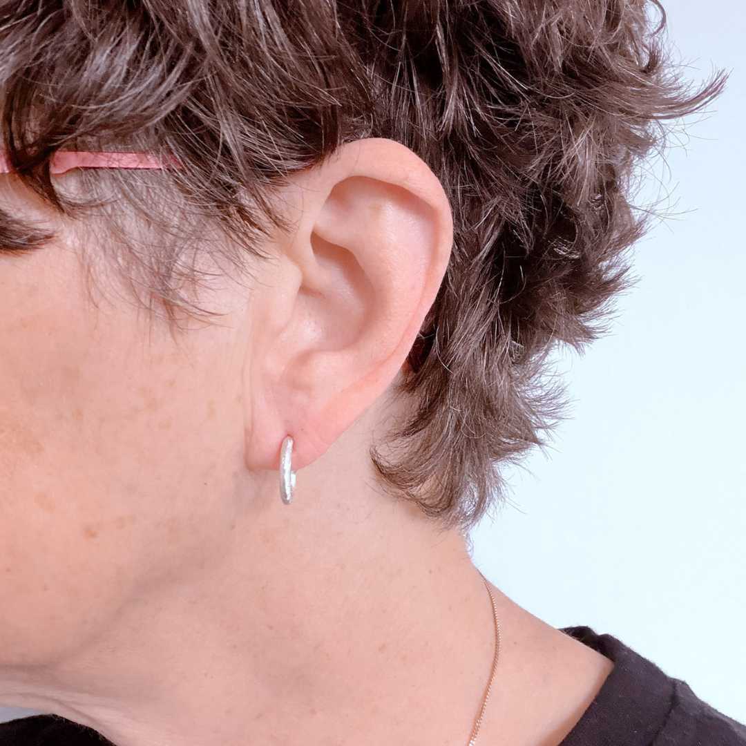 Close-up of woman with short hair wearing 14mm textured sterling silver hoop earrings showing slightly bolder fit