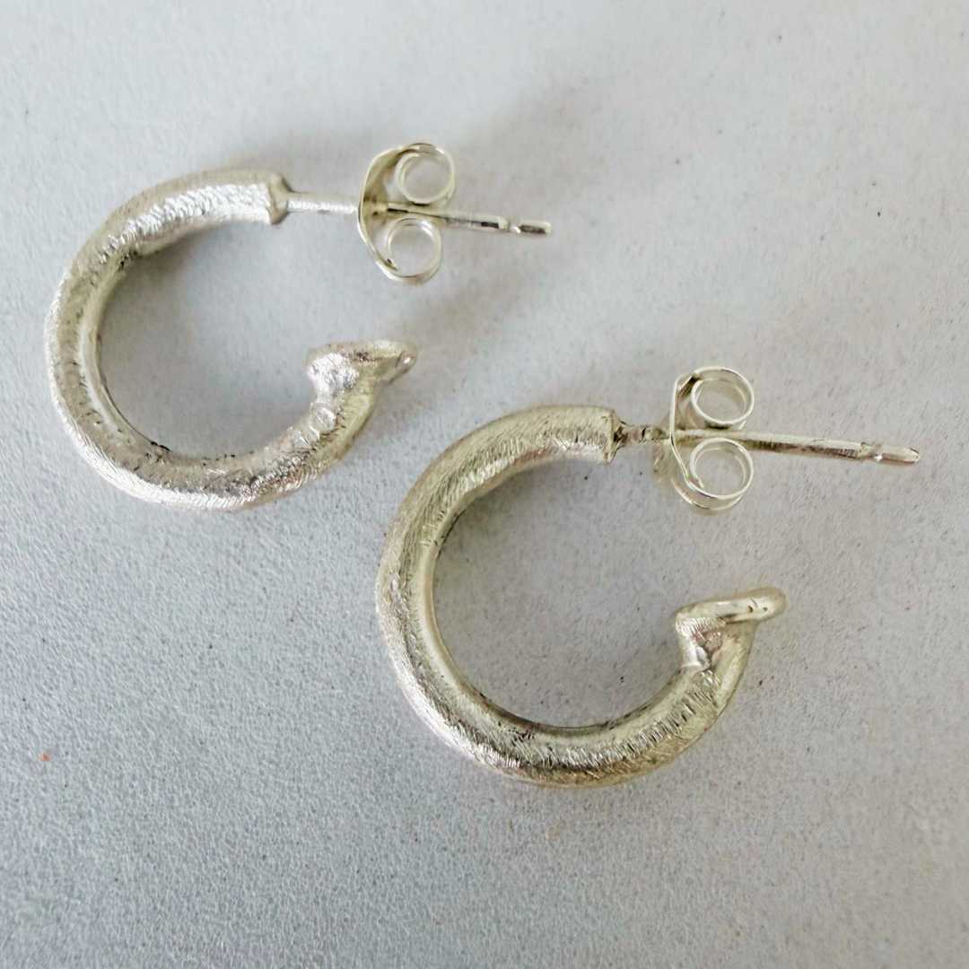 14mm textured sterling silver hoop earrings lying on grey surface viewed from above showing posts, butterflies, and hand-finished texture