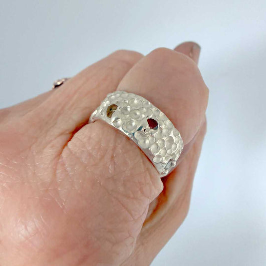 Trace Ring worn on hand, wide sterling silver band with cratered texture and seven multi-colour sapphires, size N