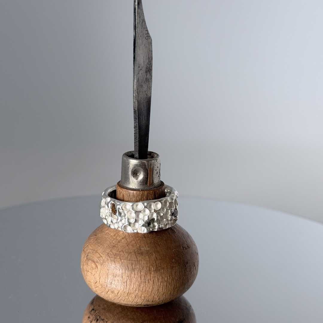 Trace Ring on graver tool showing scale and depth of textured silver band with sapphires against dark grey background