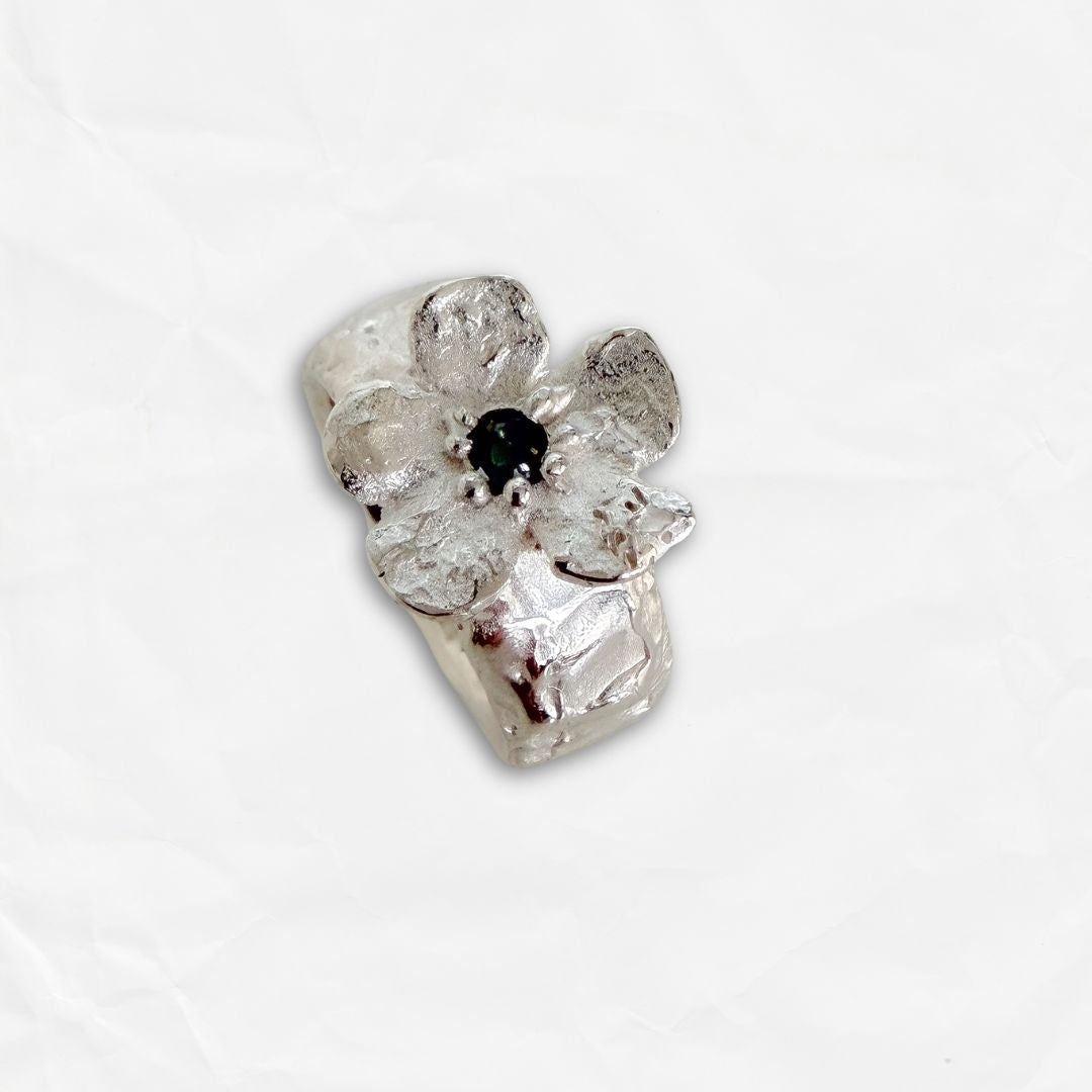 Angled view of Waiatarua Wide blue sapphire flower ring showing the irregular flower, textured petals and sculpted silver band.