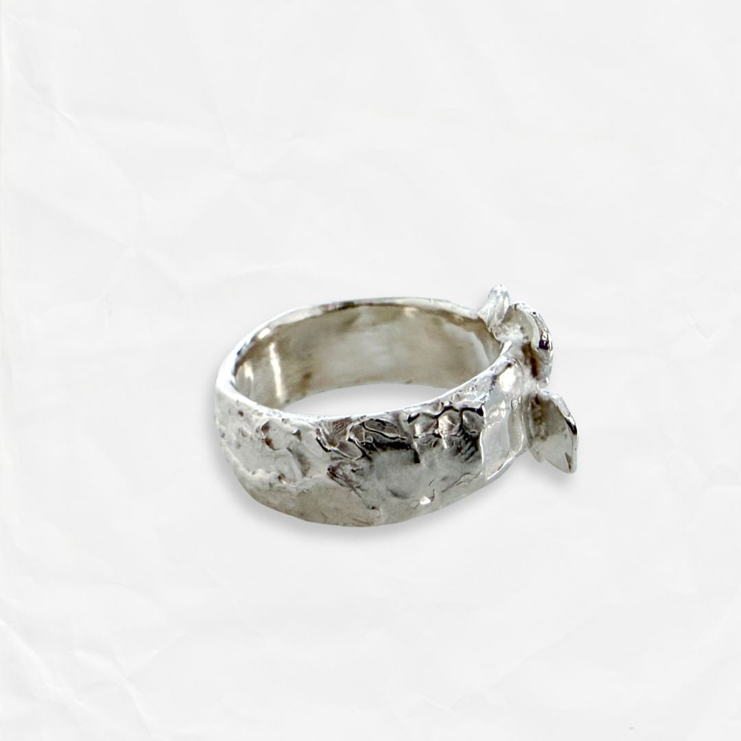 Side view of Waiatarua Wide sterling silver flower ring showing the broad textured band and sculptural flower setting.
