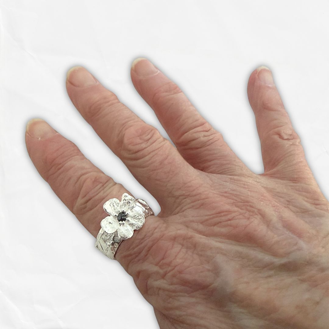 Waiatarua Wide blue sapphire flower ring worn on the hand, showing the 15mm flower and substantial 9mm textured silver band.