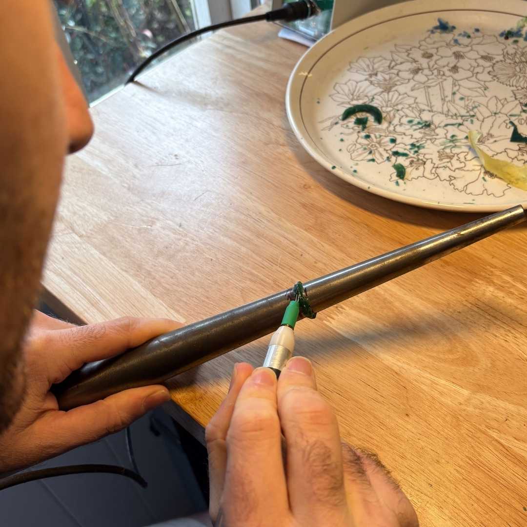 Using a wax build-up technique to drip green wax onto a mandrel during a lost wax jewellery workshop in Auckland.