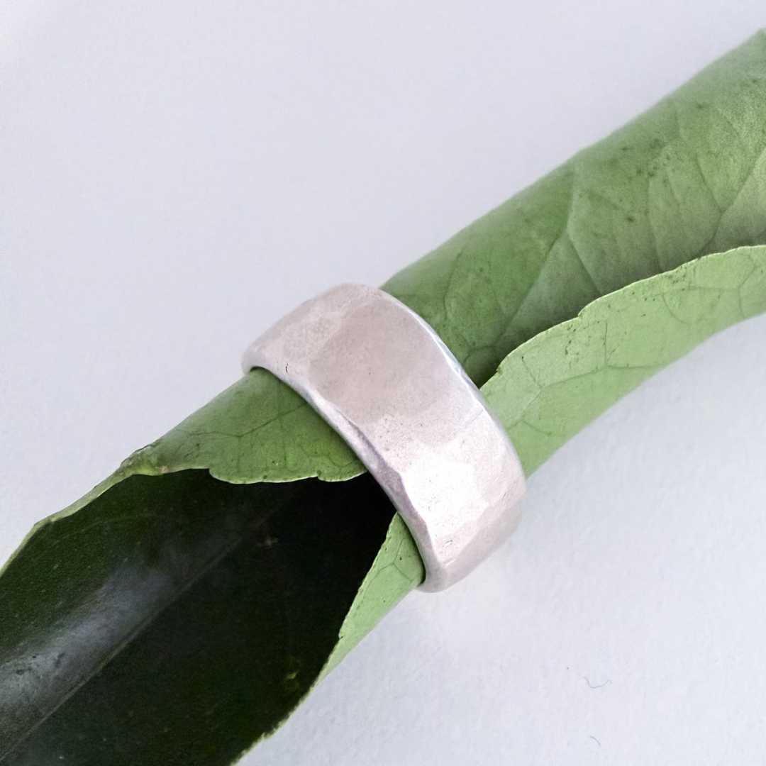 A wide, organic chunky sterling silver ring with a textured, hammered finish, size S1/2, shown wrapped around a green leaf on a plain white background.