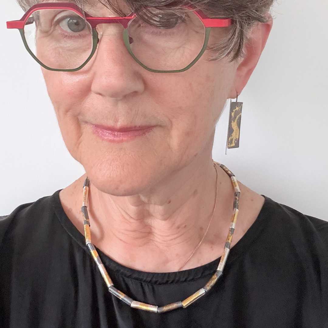 Close-up of woman wearing wrapped beaded necklace in fine silver with 24ct gold detail, showing texture against skin and matching earrings