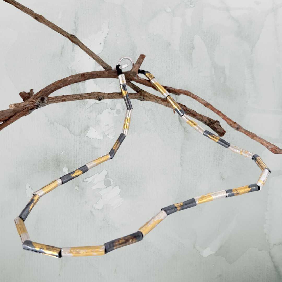 Wrapped beaded necklace in fine silver with Keum-Boo gold detail draped over a branch on soft green background