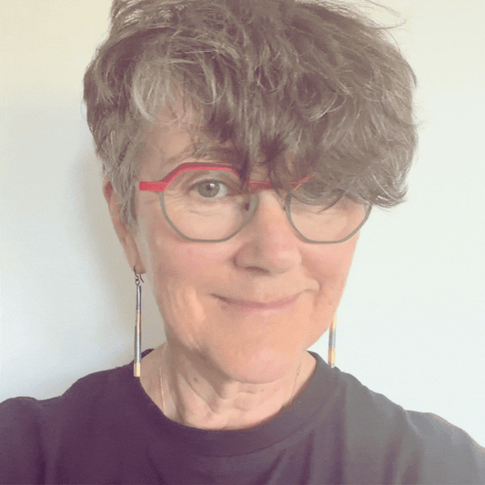 Short-haired woman with grey flecks and red-green glasses wearing long Keum-Boo pendant earrings to show how they move when worn.
