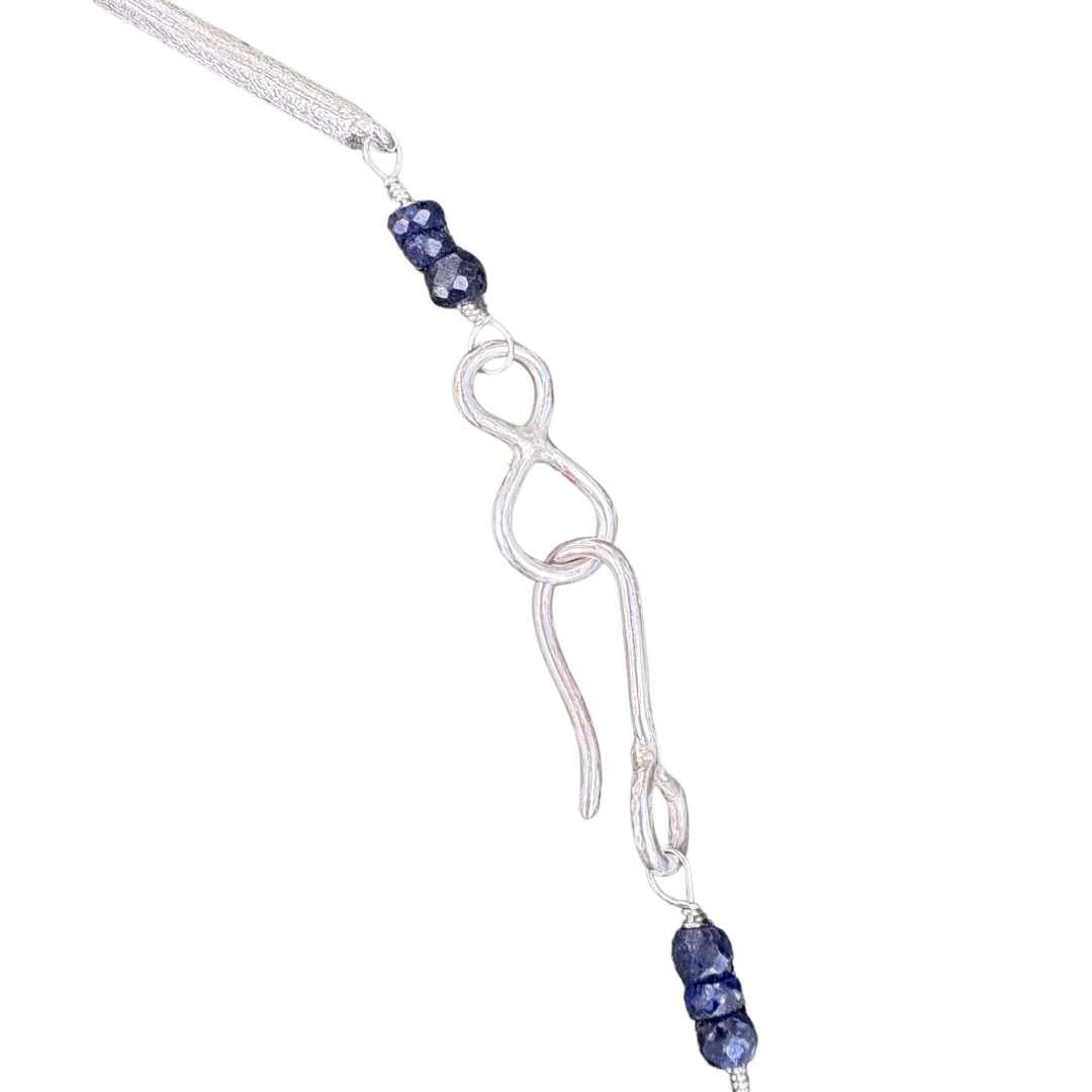Close up detail of sculptural sterling silver chain links with blue sapphire gemstones