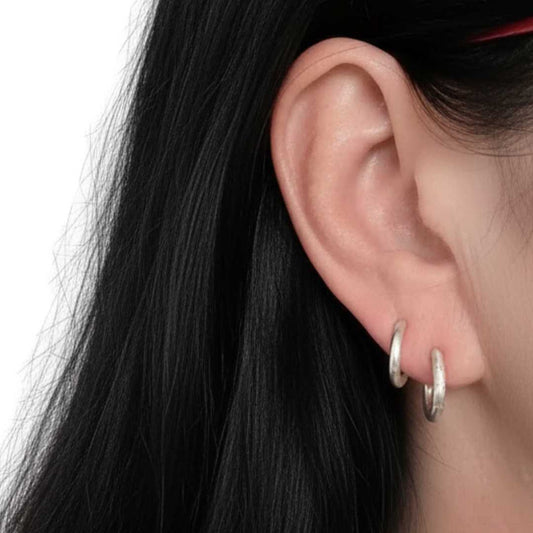 Woman with long black hair wearing textured sterling silver hoop earrings in 13mm and 14mm sizes layered in one ear stack