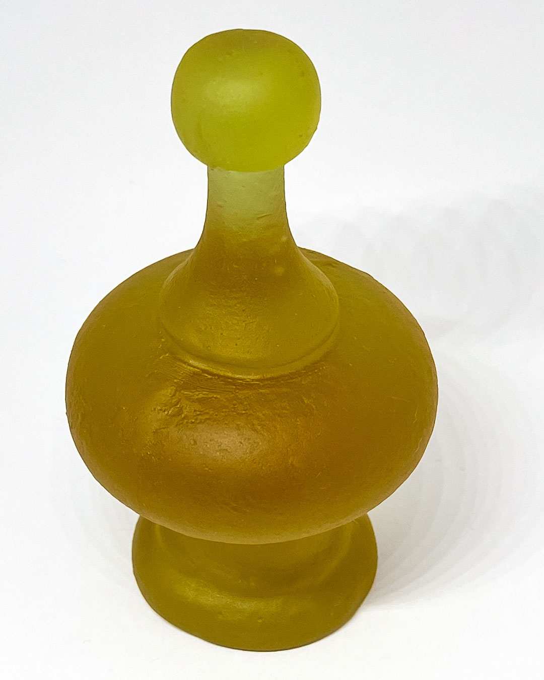 Top-down angled view of the cast glass finial in its green hue, set against a white backdrop to highlight its curved shape and translucent surface.