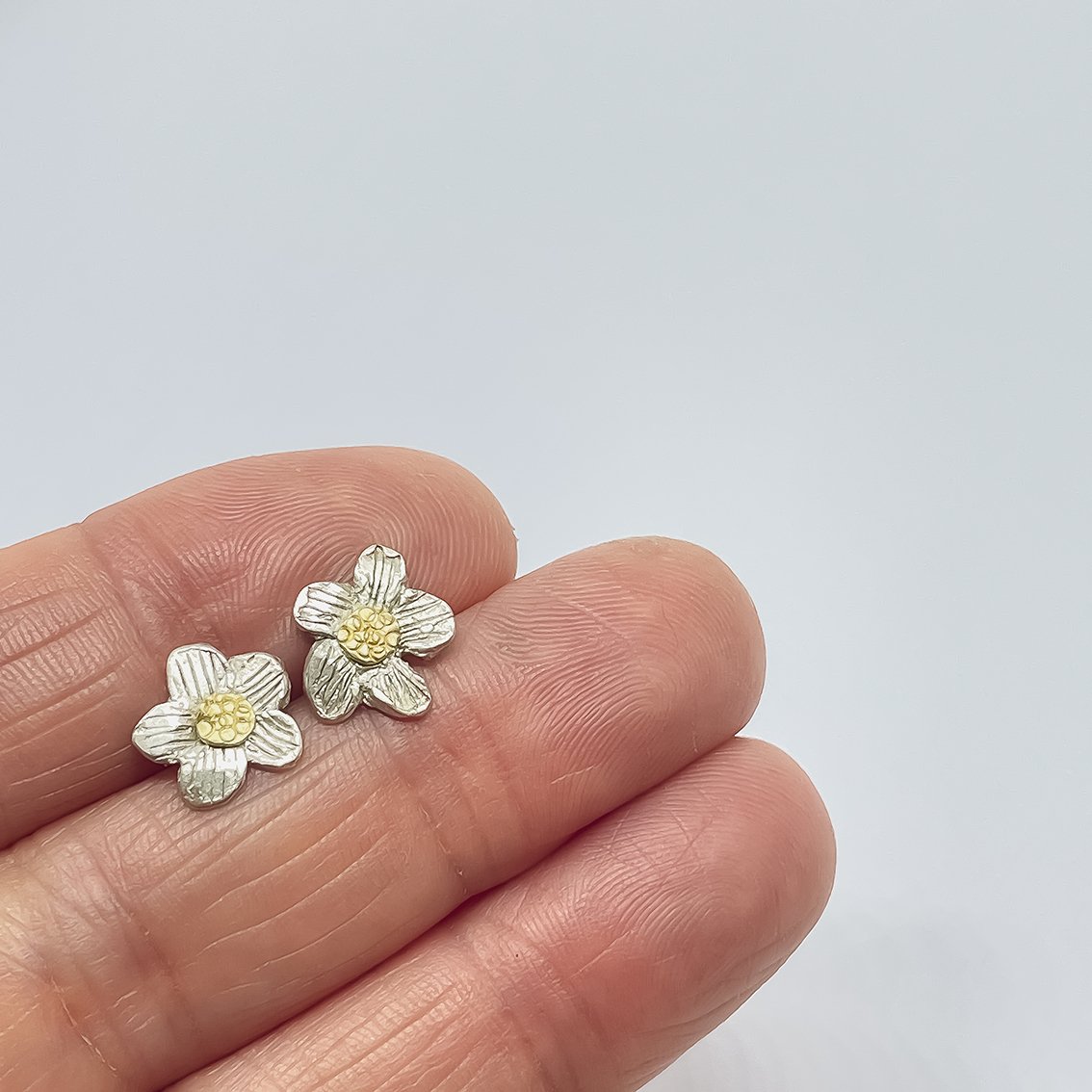 Hand holding Daisy Flower Stud Earrings in sterling silver with recycled 18ct gold centres, showing organic handmade design against a light grey background.