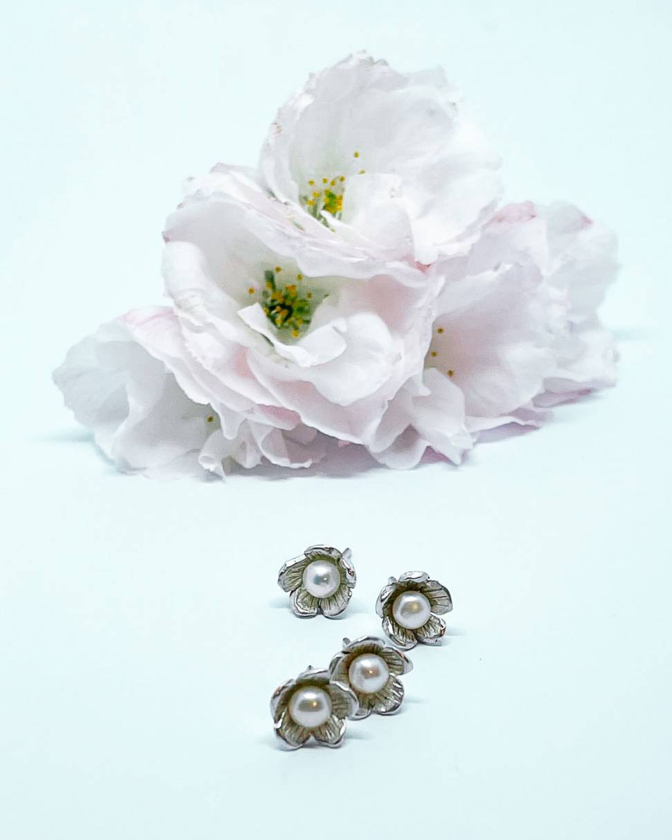 Four small flower Stud Earrings in Sterling Silver set with a white freshwater pearl, sitting in front of some blossom flowers