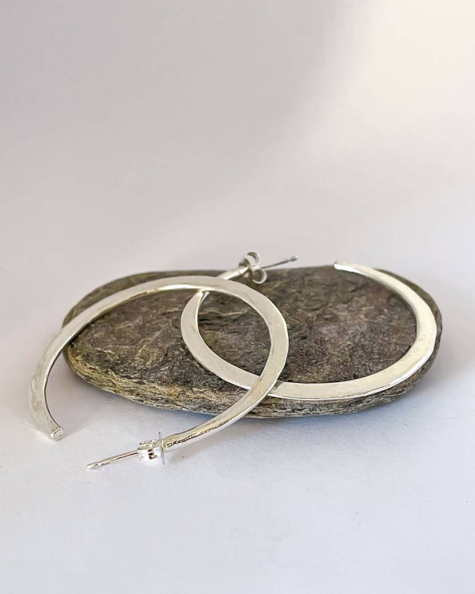 A pair of Sterling Silver Lunar Hoops showing the side profile, lying on a stone