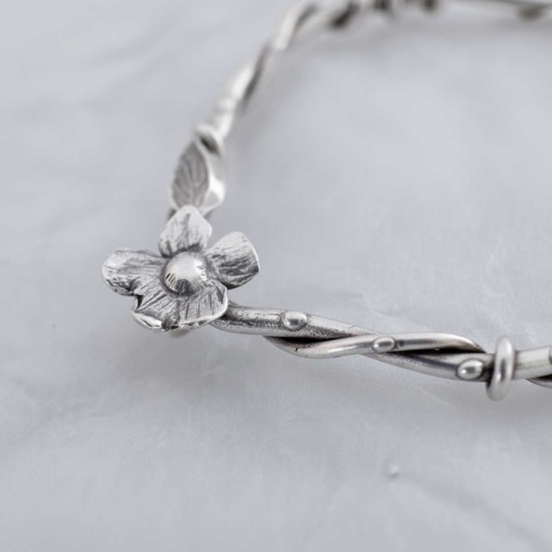 Close-up detail of handcrafted flower element on sterling silver interwoven flora statement earrings showing artisan metalwork and botanical design