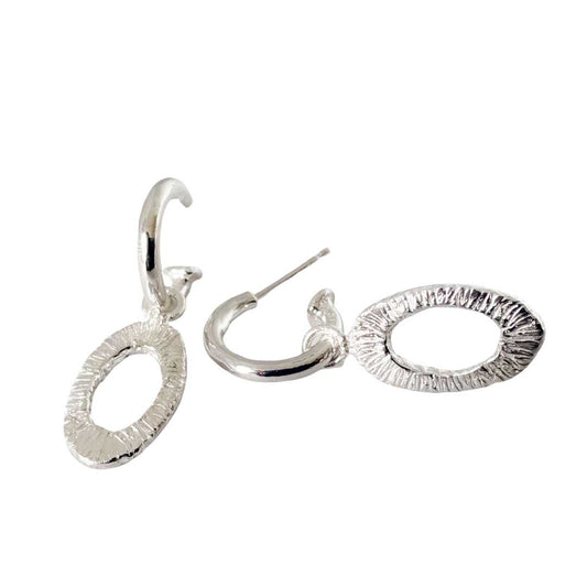 Sterling silver Oval Strata Charm Earrings shown front on and side on, with textured open oval charms hanging from polished silver hoops against a white background.