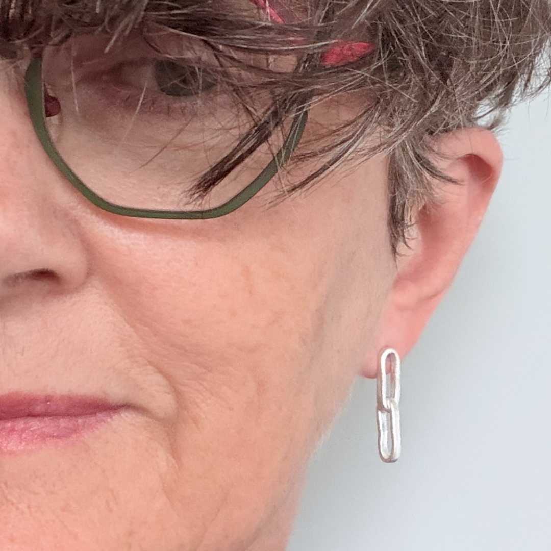 Sally Herbert wearing Paperclip Chain Link Earrings in sterling silver, styled against a light blue background